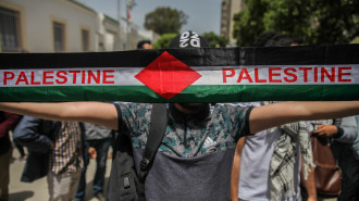 A protester lifts a Palestine scarf with the Palestinian flag during a demonstration held in front of Tunisia's parliament's building in the city of Bardo Tunis, Tunisia, on 18 May.[Getty]