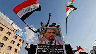 Iraqis stand next to a placard depicting renowned anti-government activist Ihab al-Wazni, who was shot dead in an ambush earlier this month, as they demonstrate in Tahrir Square in Baghdad on May 25, 2021. [Getty]