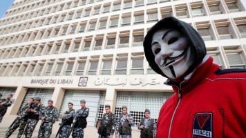 A demonstrator looks on as Lebanese policemen stand guard outside the Lebanese Central Bank in Beirut. [Getty]