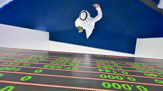 A trader walks by beneath a stock display board at the Dubai Stock Exchange in the United Arab Emirates, on 8 March, 2020. [Getty]