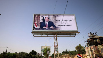 Palestinians wave Egyptian flags while sitting in a vehicle parked beneath a giant billboard depicting Egypt's President Abdel Fattah al-Sisi. [Getty]