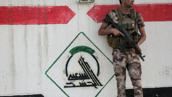 A fighter in Iraq's Popular Mobilisation Forces stands guard next to a wall showing the group's logo outside their headquarters in the capital Baghdad on 13 June, 2021. [Getty]