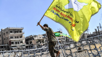 A member of the Syrian Democratic Forces (SDF), backed by US special forces, holds up his group's flag at the iconic Al-Naim square in Raqqa on 17 October 2017. [Getty]