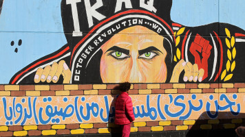 An Iraqi boy stands next to murals inspired by ongoing anti-government demonstrations in the Iraqi capital Baghdad's Tahrir square on 14 January 2020. [Getty]