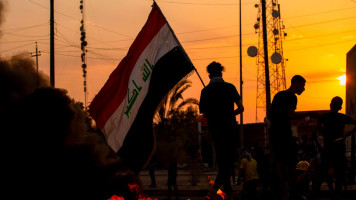 A demonstrator waves the national flag during a protest in the southern city of Basra on July 14, 2020, as they block the road to denounce the lack of electricity and services. [Getty]