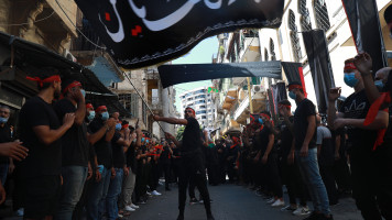 A man hoists a flag as onlookers clap during the "al-Nabda" Ashura commemoration. (TNA)