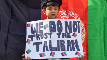 A young boy stands next to a flag of Afghanistan and holds a placard which says 'We Do Not Trust The Taliban' during the demonstration in Parliament Square. [Getty]