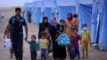 An Iraqi family walks past tents at a temporary camp set up to shelter Iraqis fleeing violence in Iraq's northern Nineveh province on June 12, 2014, in Aski kalak, 40 kms West of Arbil. [Getty]