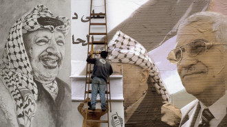 Workers post an election poster of PLO chairman Mahmoud Abbas with a picture of late leader Yasser Arafat in the northern West Bank city of Nablus, 25 December 2004. [Getty]