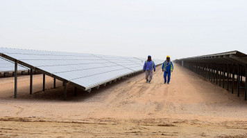 Employees walk past solar panels at the Mohammed bin Rashid Al-Maktoum Solar Park on March 20, 2017, in Dubai. Dubai completed a solar plant big enough to power 50,000 homes as part of a plan to generate three-quarters of its energy from renewables by 2050. / AFP PHOTO / STRINGER (Photo credit should read STRINGER/AFP via Getty Images)