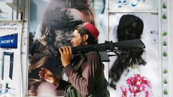 A Taliban fighter walks past a beauty salon with images of women defaced using spray paint in Shar-e-Naw in Kabul on August 18, 2021. (Photo by Wakil KOHSAR / AFP) (Photo by WAKIL KOHSAR/AFP via Getty Images)