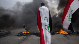 An Iraqi demonstrator clad with the national flag stands in front of burning tyres blocking a street amid a general strike in the southern city of Basra, on November 25, 2019