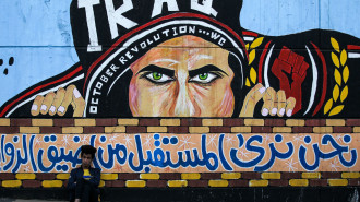 An Iraqi youth sits leaning on a wall with a graffiti mural showing a protester with text in Arabic reaing "we see the future from the narrowest angles", at the anti-government sit-in in the capital's Tahrir Square on December 24, 2019