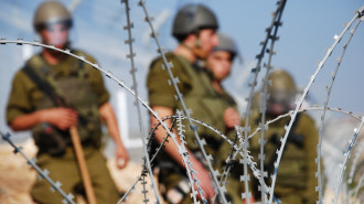 Four Israeli soldiers stand behind razor wire near the Palestinian village of Bil'in in the West Bank