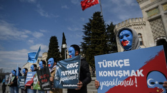 Demonstrators wearing a mask painted with the colours of the flag of East Turkestan hold placards reading "Speaking Turkish , banned" and "fasting in ramadan, banned" during a protest by supporters of the Uighur minority on April 1, 2021 at beyazid square in Istanbul [Getty Images]