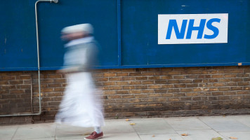 Person walks past a sign for the NHS or National Health Service in London, UK. The National Health Service (NHS) is the shared name of three of the four publicly funded healthcare systems in the United Kingdom [Getty Images]