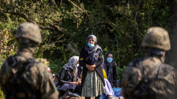 Polish border guards stand next to migrants believed to be from Afghanistan sit on the ground in the small village of Usnarz Gorny near Bialystok, northeastern Poland, located close to the border with Belarus, on August 20, 2021