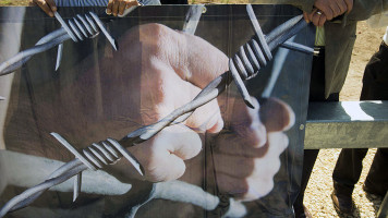 Palestinians holding a banner which has a person holding prison bars with barbed wire overlaid