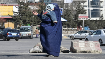 Afghan woman carrying her child begs on street