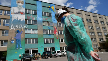 A woman wearing personal protective equipment (PPE) stands in front of a graffiti painted on Lviv emergency hospital wall, to thanks the medical staff and healthcare fighting against the spread of the COVID-19 coronavirus on June 30, 2020. - 