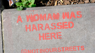 The words 'A woman was harassed here' is seen stenciled onto a raised stone flower bed in a street 