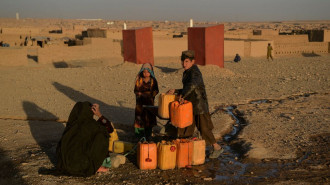 This picture taken on October 13, 2021, shows a woman and children filling tanks with water at the Shahrak Sabz Internally Displaced People (IDP) camp in Herat province. - Drought stalks the parched fields around the remote Afghan district of Bala Murghab, where climate change is proving a deadlier foe than the country's recent conflicts.