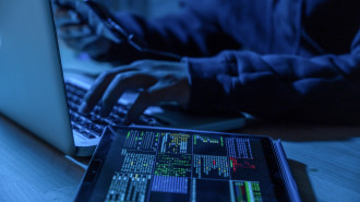 A hacker typing on a laptop with, holding a tablet with a second on the table