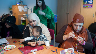 A group of Muslim mothers concentrate on threading beads during a craft workshop for parents at Marner Primary School in Tower Hamlets