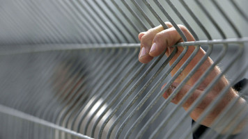 A woman's hand gripping onto a metal fence at the Ofer military base in Palestine's occupied West Bank