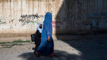 In this picture taken on August 9, 2022, an Afghan woman and a girl walk to a primary school in Kabul