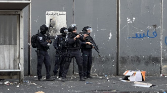 Israeli policeman aims weapon at Palestinian protesters inside the Shuafat refugee camp, on 12 October 2022. [Ibrahim Husseini/TNA]