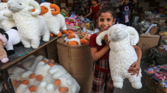 A girl holds a fluffy plush sheep toy near a toy stand at the market place before the upcoming Eid al-Adha 