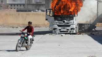 A man rides a motorcycle near a burning Turkish truck during protests against Turkey in al-Bab, in the northern Syrian opposition held region of Aleppo on July 1, 2024. 