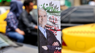 Motorists drive past an election poster for Iranian presidential candidate Masoud Pezeshkian