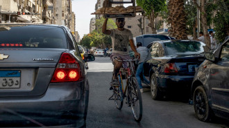 A deliveryman balances a tray of freshly baked bread while riding his bicycle through traffic in central Cairo on May 17, 2024