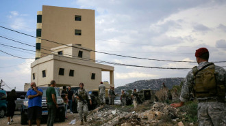 Men in military uniform inspect a site as civilians stand nearby 