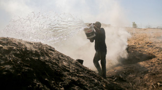 A worker pours water over a coal pit, sending up clouds of steam in Khan Younis, Gaza, on October 31, 2024. Palestinian workers labor in a coal-making pit amid the challenging living conditions faced by displaced Palestinians in the southern Gaza Strip.