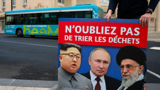 An employee holds a poster bearing portraits of (From L) North Korea's leader Kim Jong Un, Russia's President Vladimir Putin and Iran's Supreme Leader Ali Khamenei with a slogan which reads in French "Don't forget to sort the waste" after removing it from a city bus in Béziers, southern France on January 9, 2025.