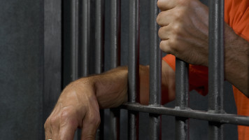 A prisoner standing behind his prison cell bars