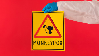 A red triangle sign with a monkey in the middle on a yellow background. Below reads the text: "Monkeypox."