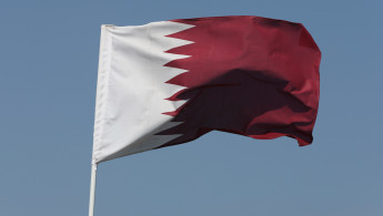 The National Flag Of Qatar Flying Against A Blue Sky