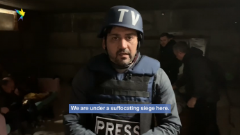 A reporter speaking to camera with the caption: "We are under a suffocating siege here."