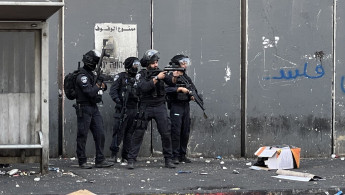 Israeli policeman aims weapon at Palestinian protesters inside the Shuafat refugee camp, on 12 October 2022. [Ibrahim Husseini/TNA]