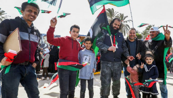 Libyans wave national flags during a parade in the coastal city of Tajura to commemorate the anniversary of the demonstration that toppled Gaddafi [Getty]