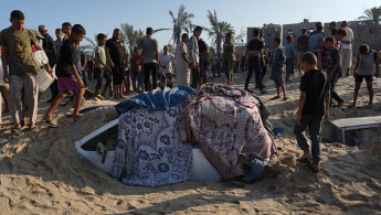 Palestinians stand next to a car covered in sand at the site of Israeli strikes on a makeshift displacement camp in Mawasi Khan Yunis in the Gaza Strip on September 10, 2024.