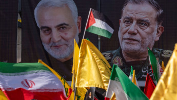 Iranian people wave a Palestinian, Iranian, and Hezbollah flags in front of portraits of IRGC Generals Qassem Soleimani and Abbas Nilforoushan, during a gathering in Tehran