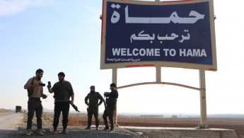 Armed groups, opposing Syria's Bashar al-Assad regime, are seen in front of a sign for the city of Hama, on 3 December 2024