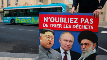 An employee holds a poster bearing portraits of (From L) North Korea's leader Kim Jong Un, Russia's President Vladimir Putin and Iran's Supreme Leader Ali Khamenei with a slogan which reads in French "Don't forget to sort the waste" after removing it from a city bus in Béziers, southern France on January 9, 2025.