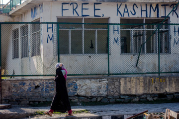 A Kashmiri Muslim woman walks past graffiti saying 'free Kashmir' 