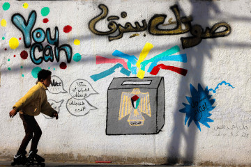 A Palestinian boy rollerblades past an election mural in Gaza City on 28 April, 2021. [Getty]